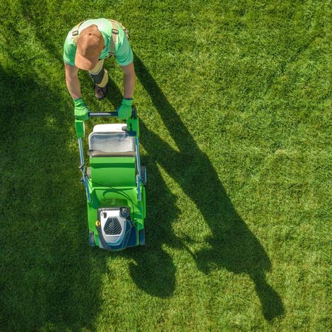 GREEN CANYON LANDSCAPING INC | A man is mowing a lush green lawn with a green lawn mower.