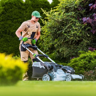 GREEN CANYON LANDSCAPING INC | A man is pushing a lawn mower on a lush green lawn.