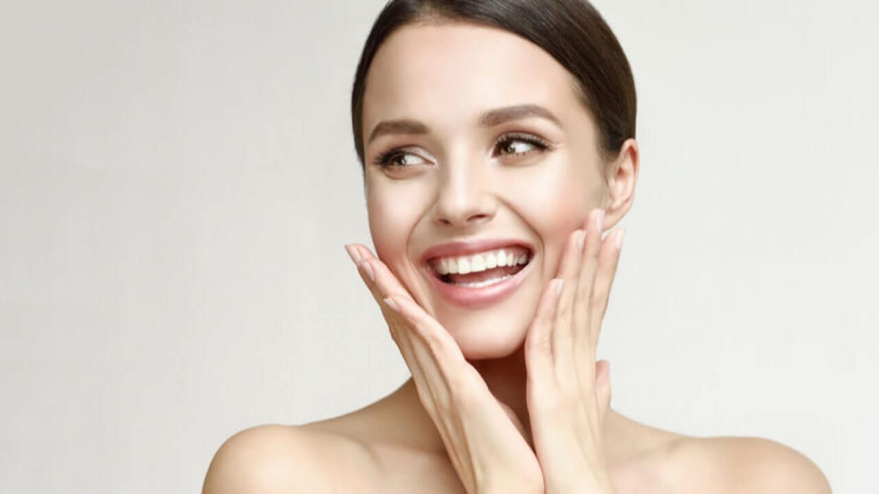 Uma mulher está sorrindo e tocando o rosto com as mãos.