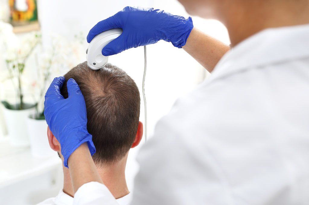 Um médico está examinando o cabelo de um homem com um aparelho.