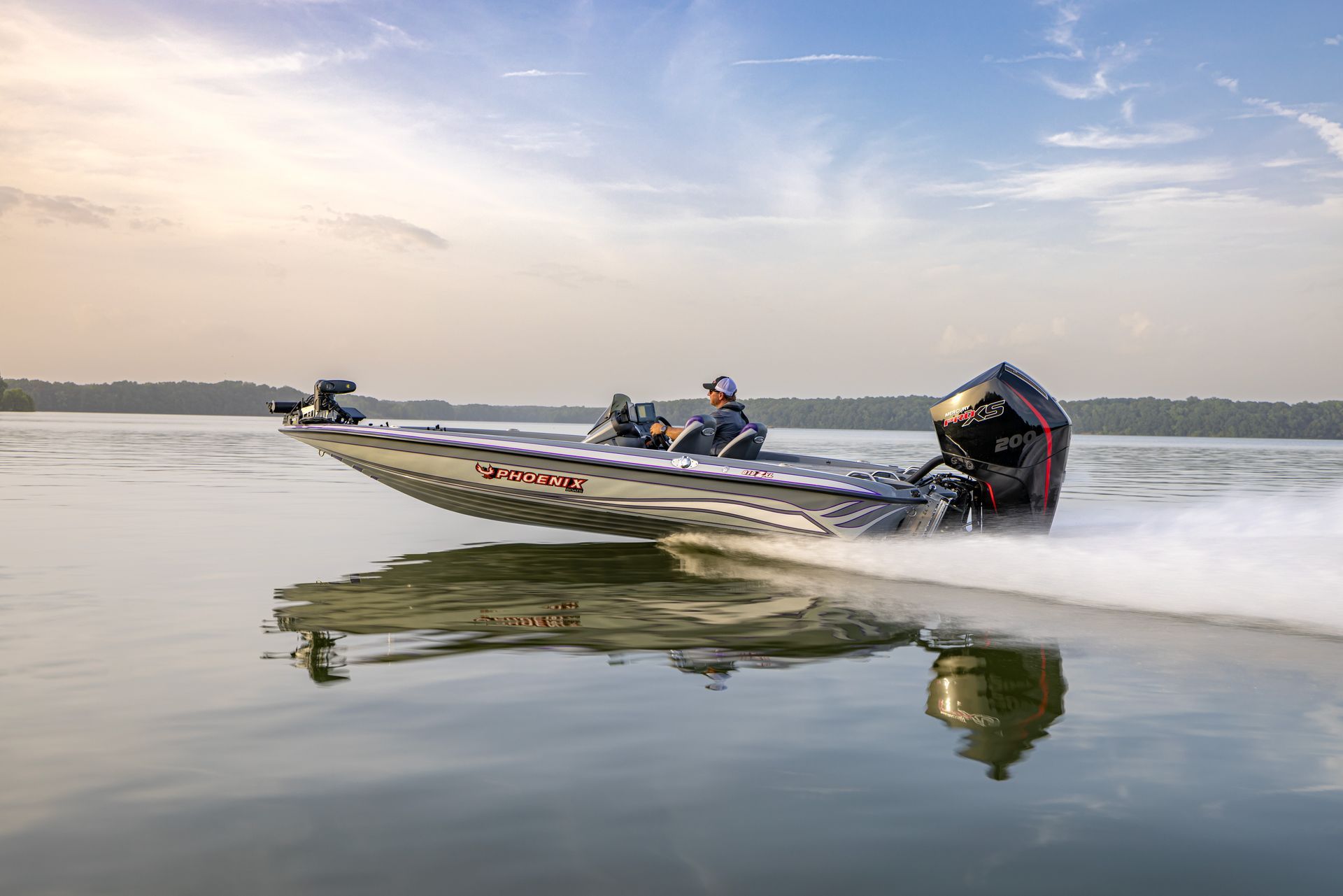 A bass fishing boat speeding on a lake with two people on board under a cloudy sky.