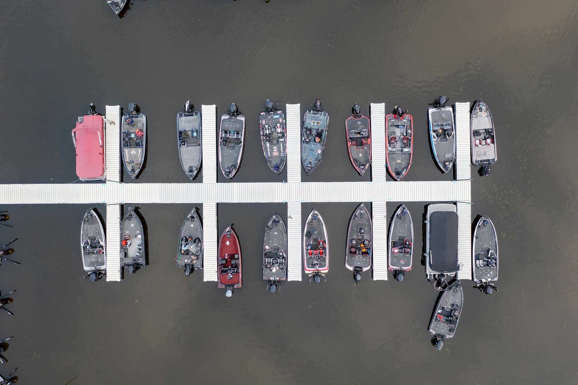 An aerial view of many small fishing boats docked on both sides of a long white pier in the water.