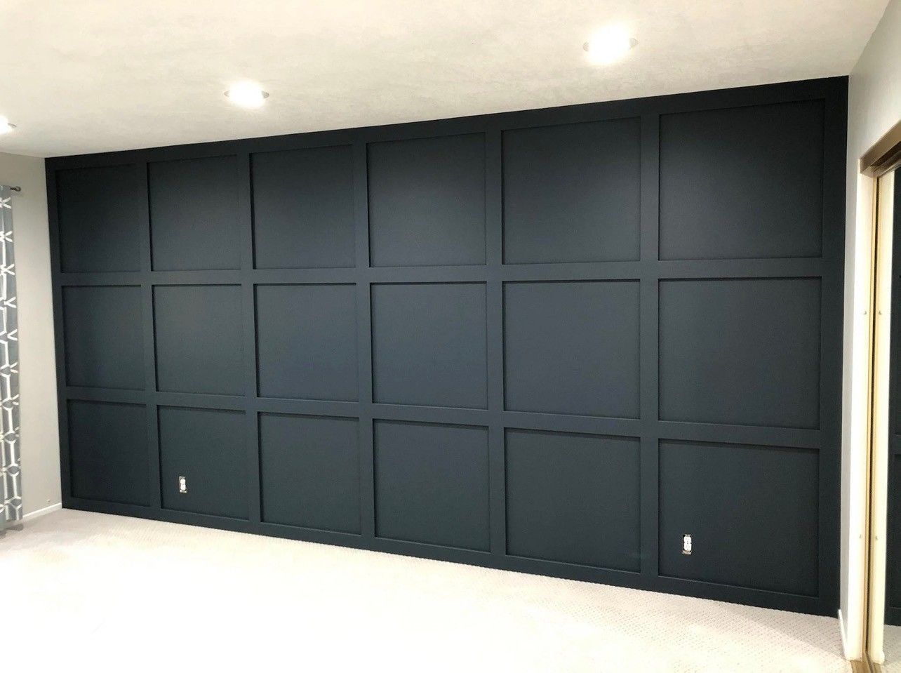 Dark paneled wall with recessed square sections in a bright, empty room