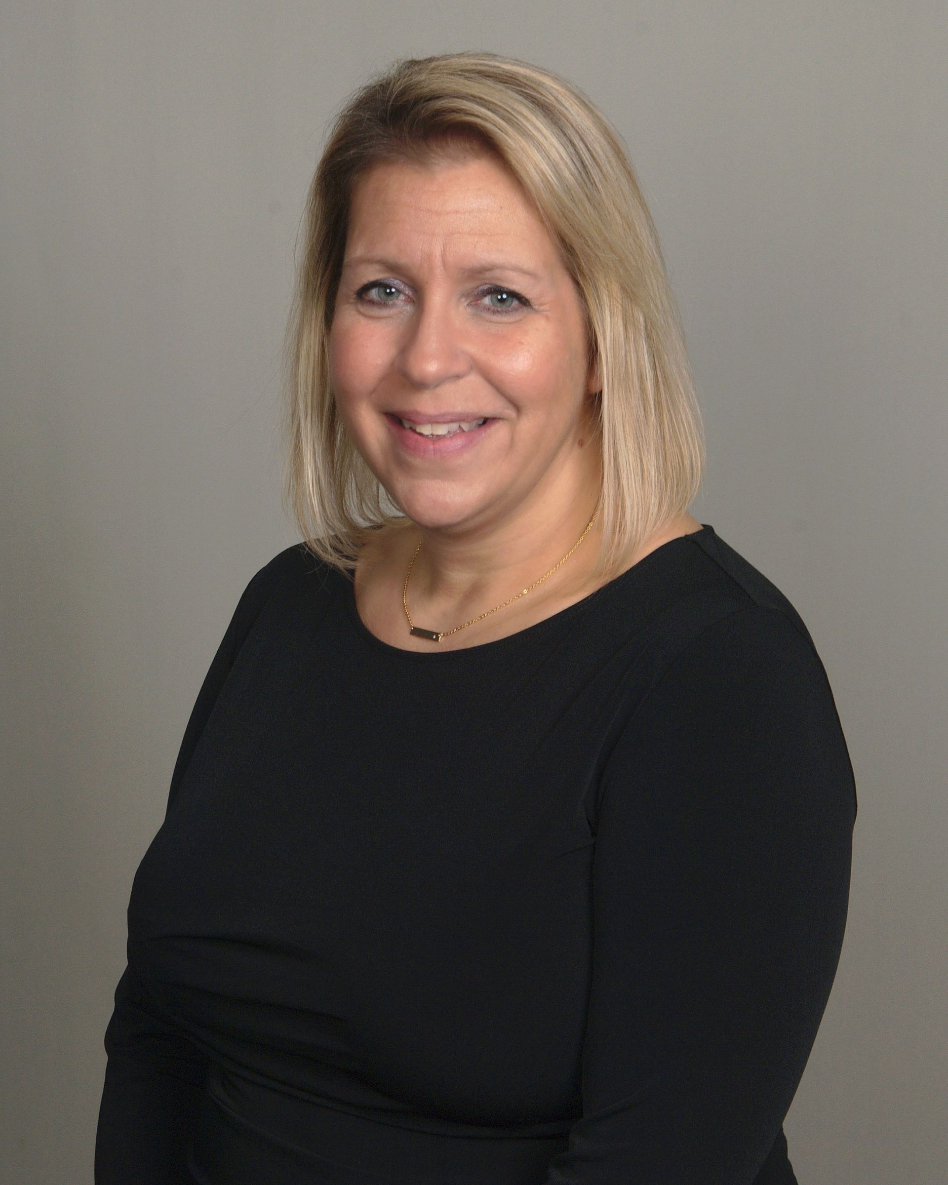 A woman wearing a gray jacket and a purple shirt is smiling for the camera.