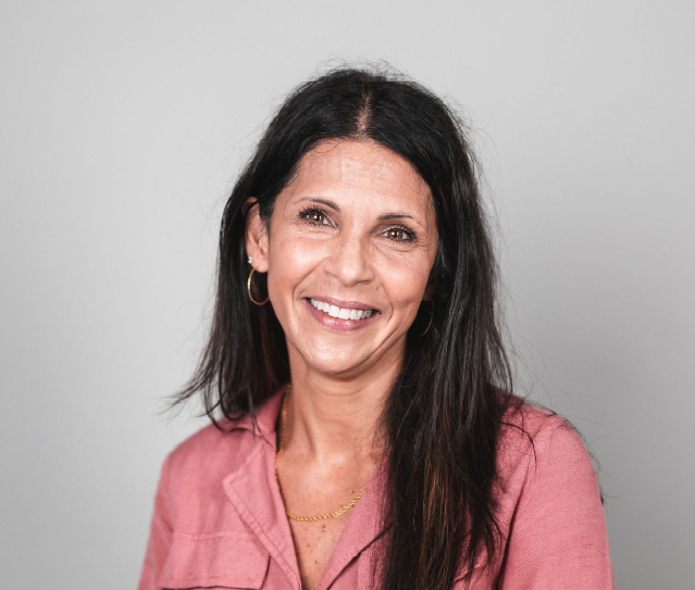 A woman wearing a gray jacket and a purple shirt is smiling for the camera.