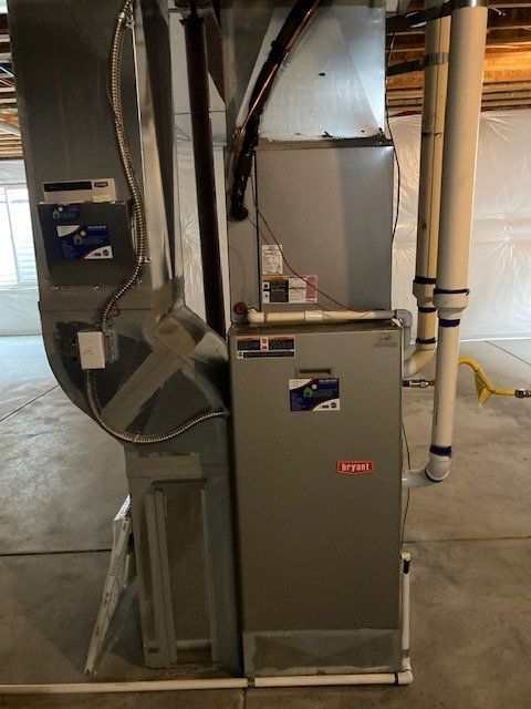 Furnace with ductwork in a basement. The unit is gray and metallic. White PVC pipes are adjacent.