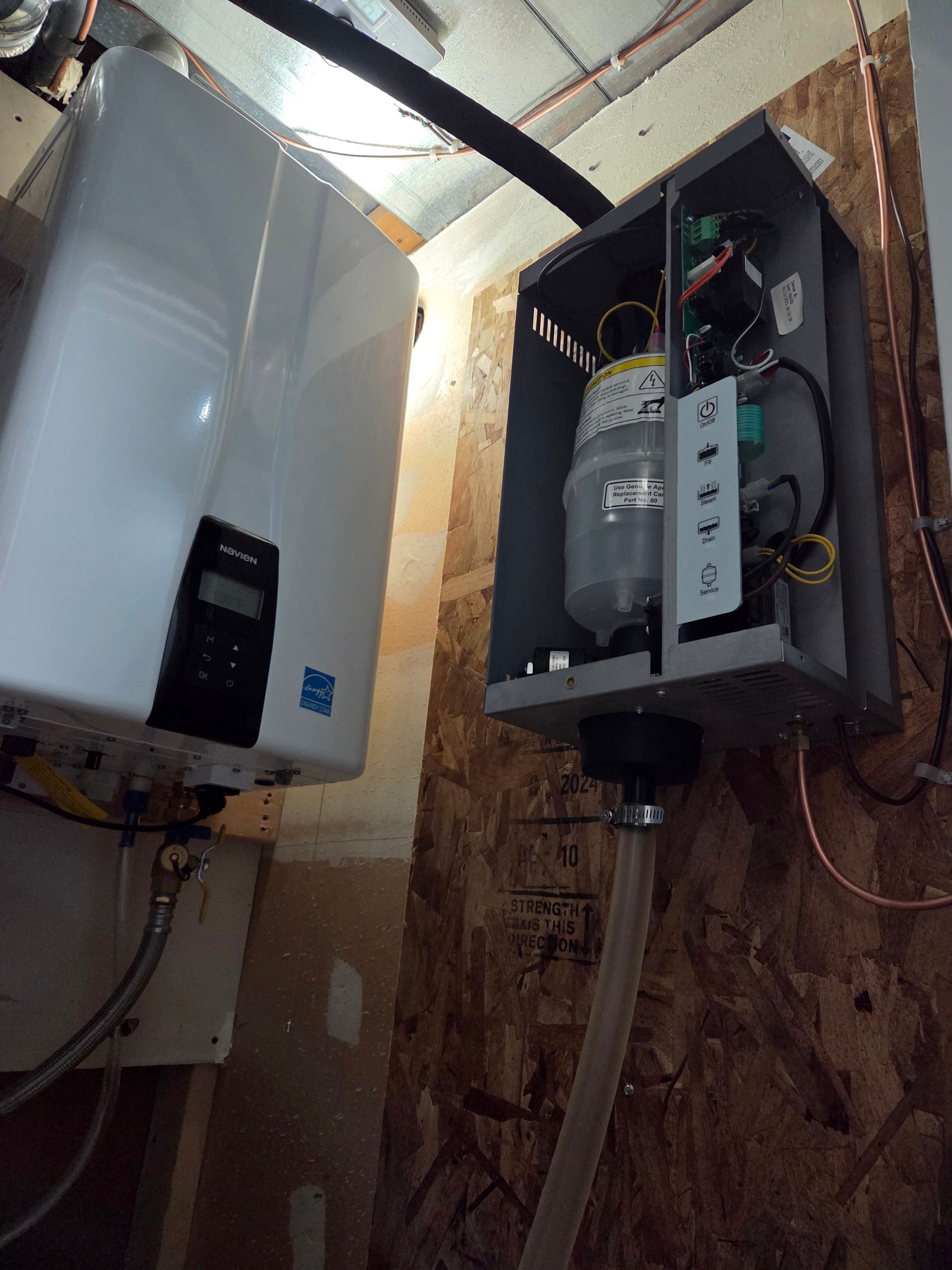 Two white water heaters mounted on a wooden wall, one with an open panel revealing interior components.