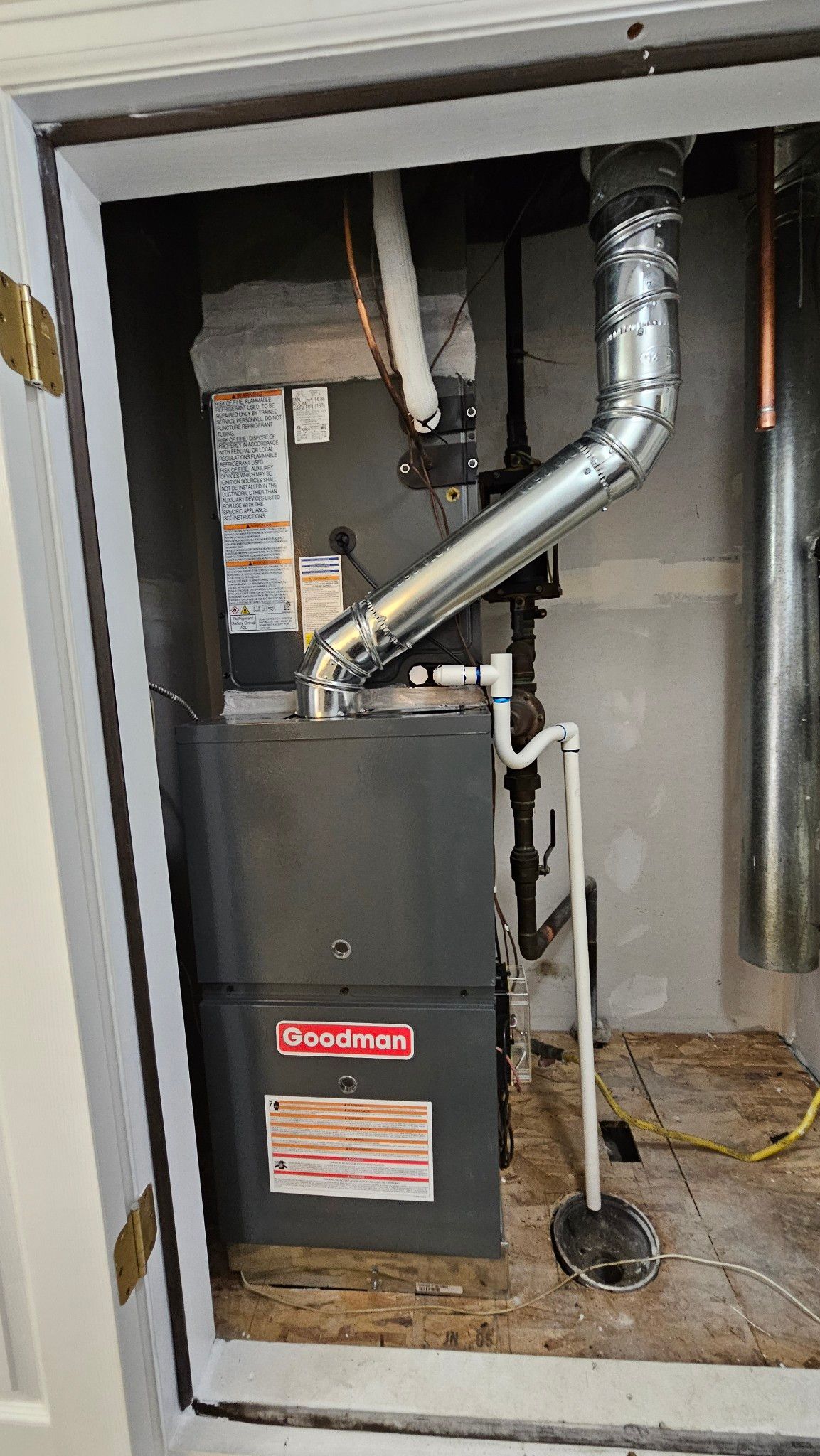 Furnace unit in a small utility room. Gray Goodman furnace with vent and pipes.