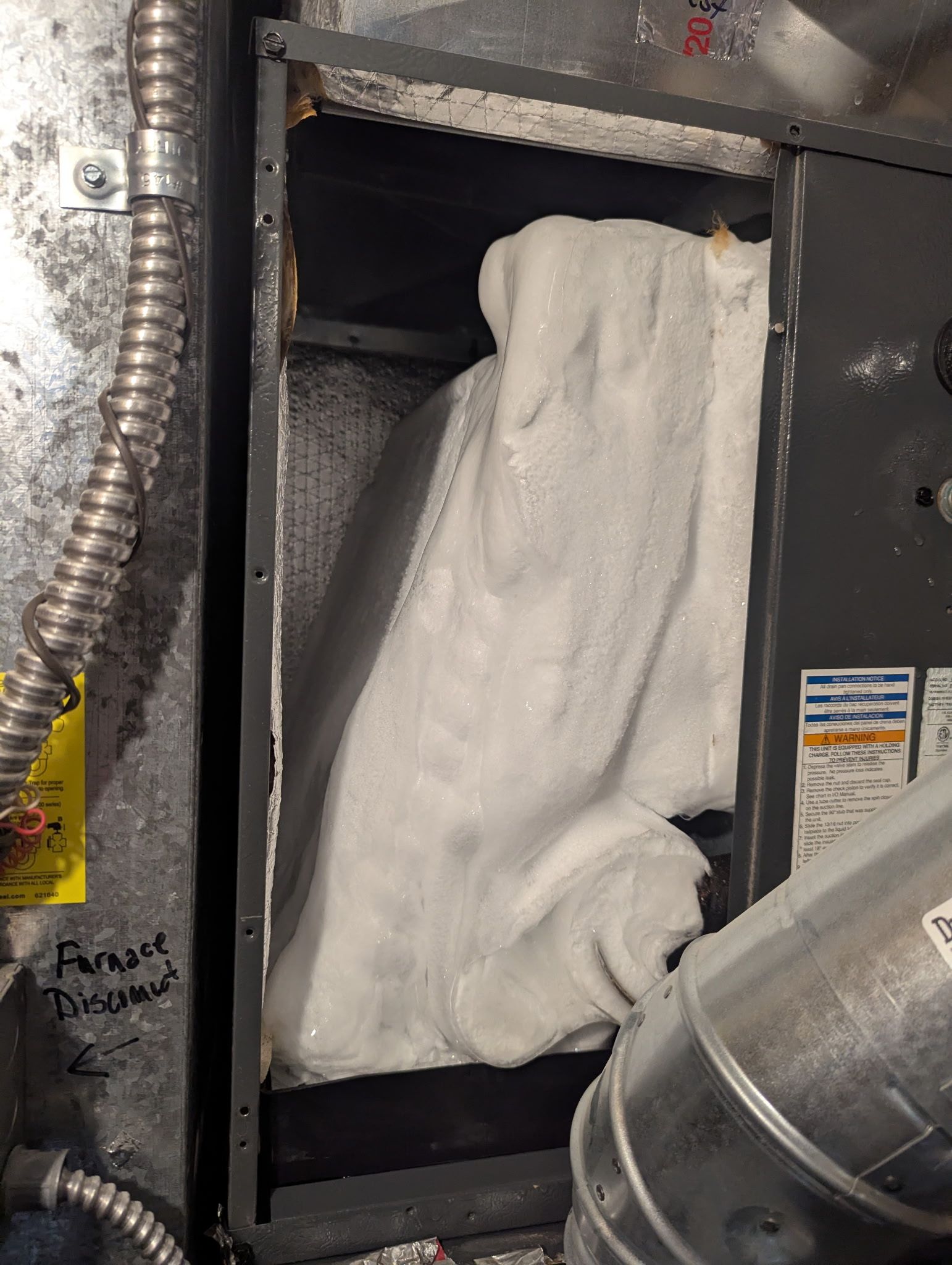 Furnace filter within a metal box. White, rectangular filter is visible. Silver ductwork and wires also shown.