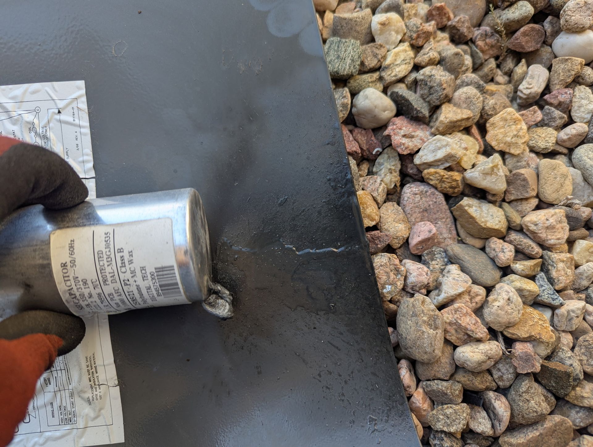 Gloved hand holding a metal can over a black surface, near rocks.