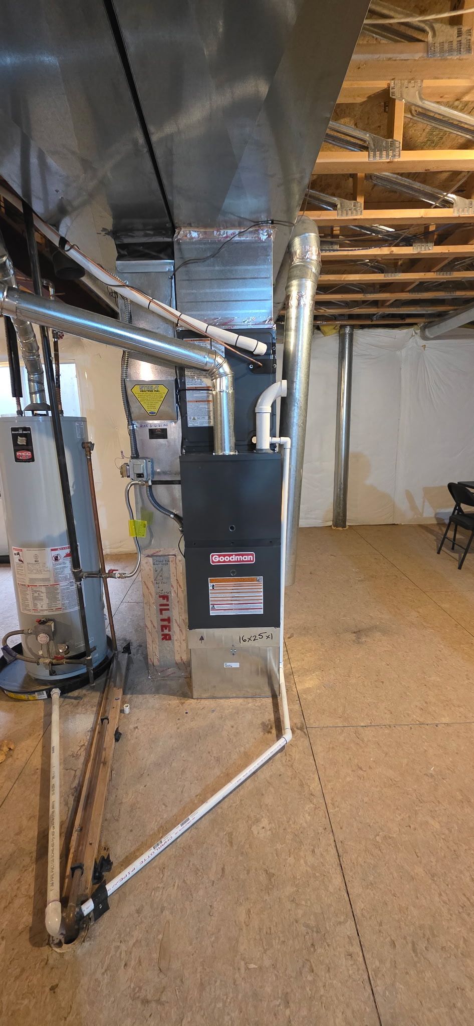 Furnace and water heater in a basement. Metal ductwork and pipes are visible. Wooden beams on the ceiling.