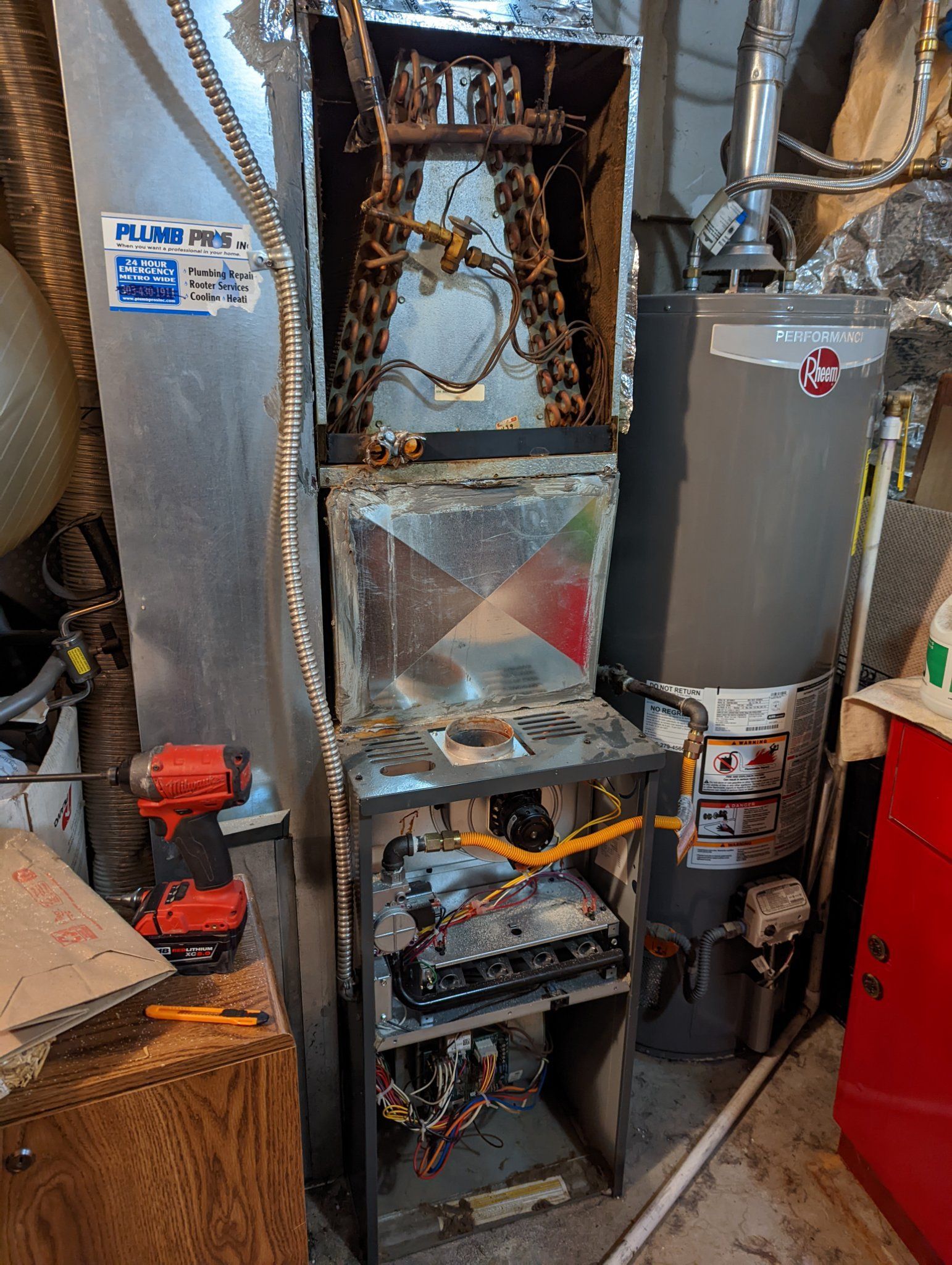 Damaged furnace with exposed components, near a water heater and electrical tools, in a basement setting.