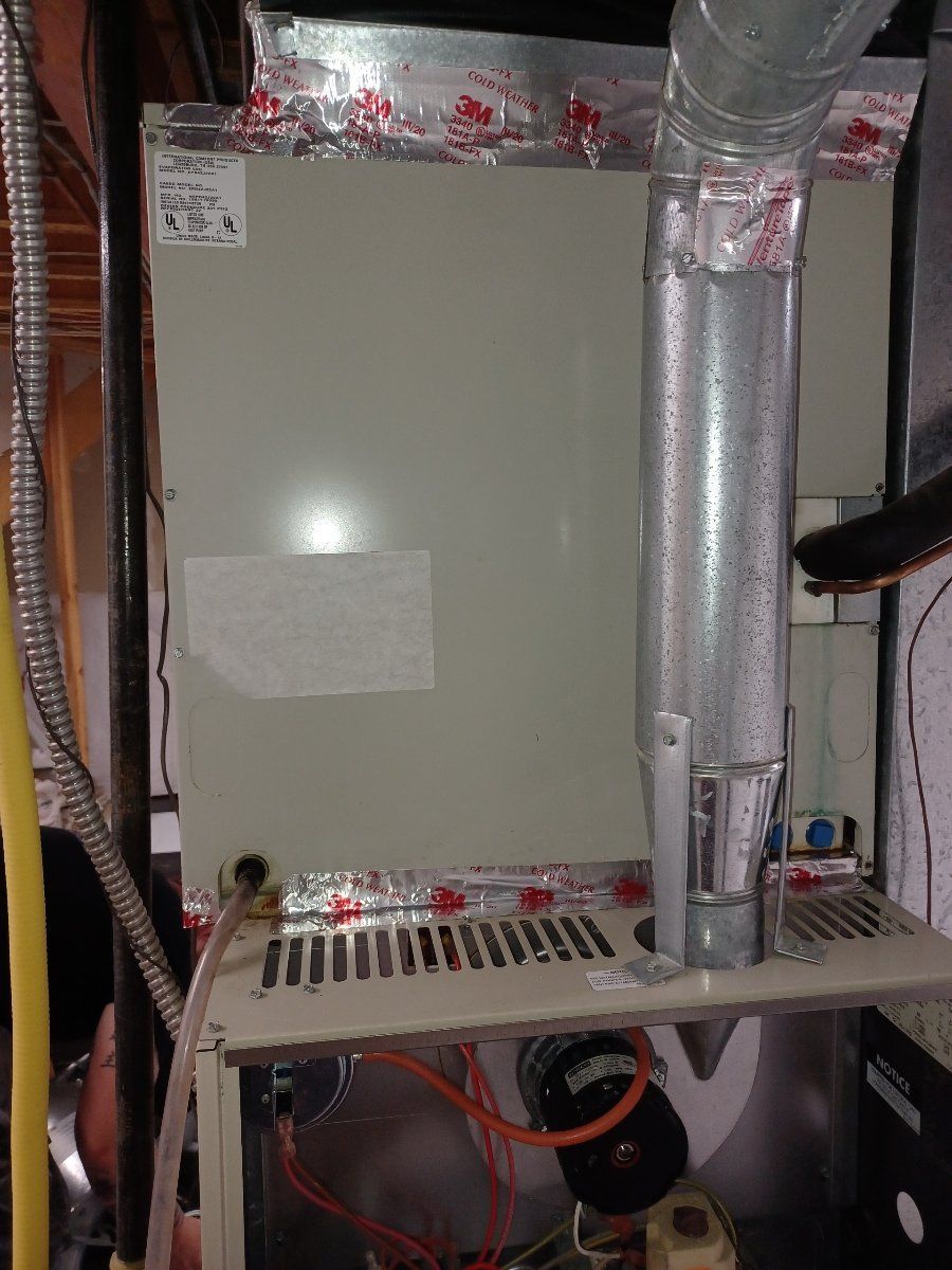 Furnace in a basement, light gray metal, with silver ductwork and various tubes and wires.