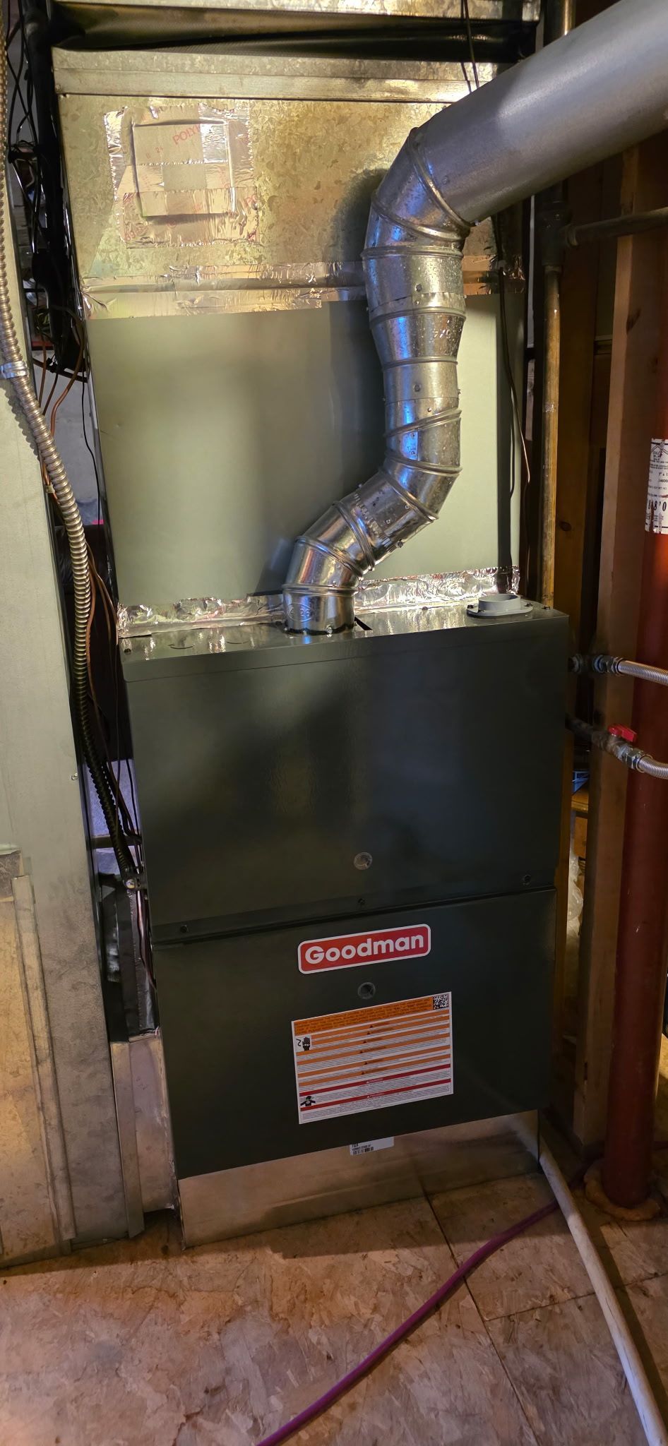 A dark furnace with silver ductwork in a basement setting.