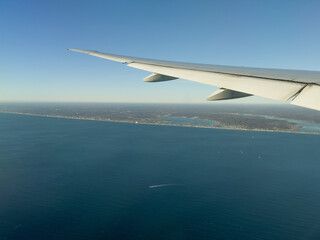 The wing of an airplane is flying over the ocean.