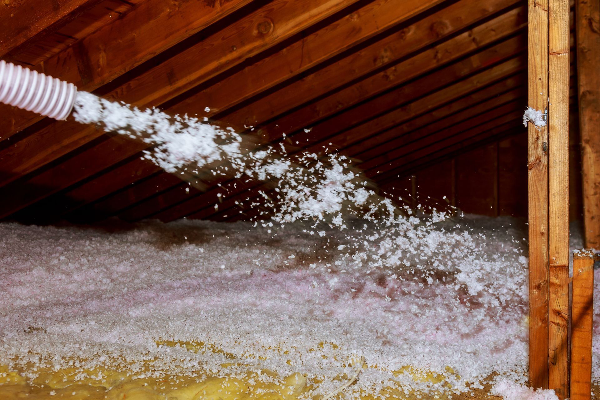 A person is blowing insulation into an attic with a hose.