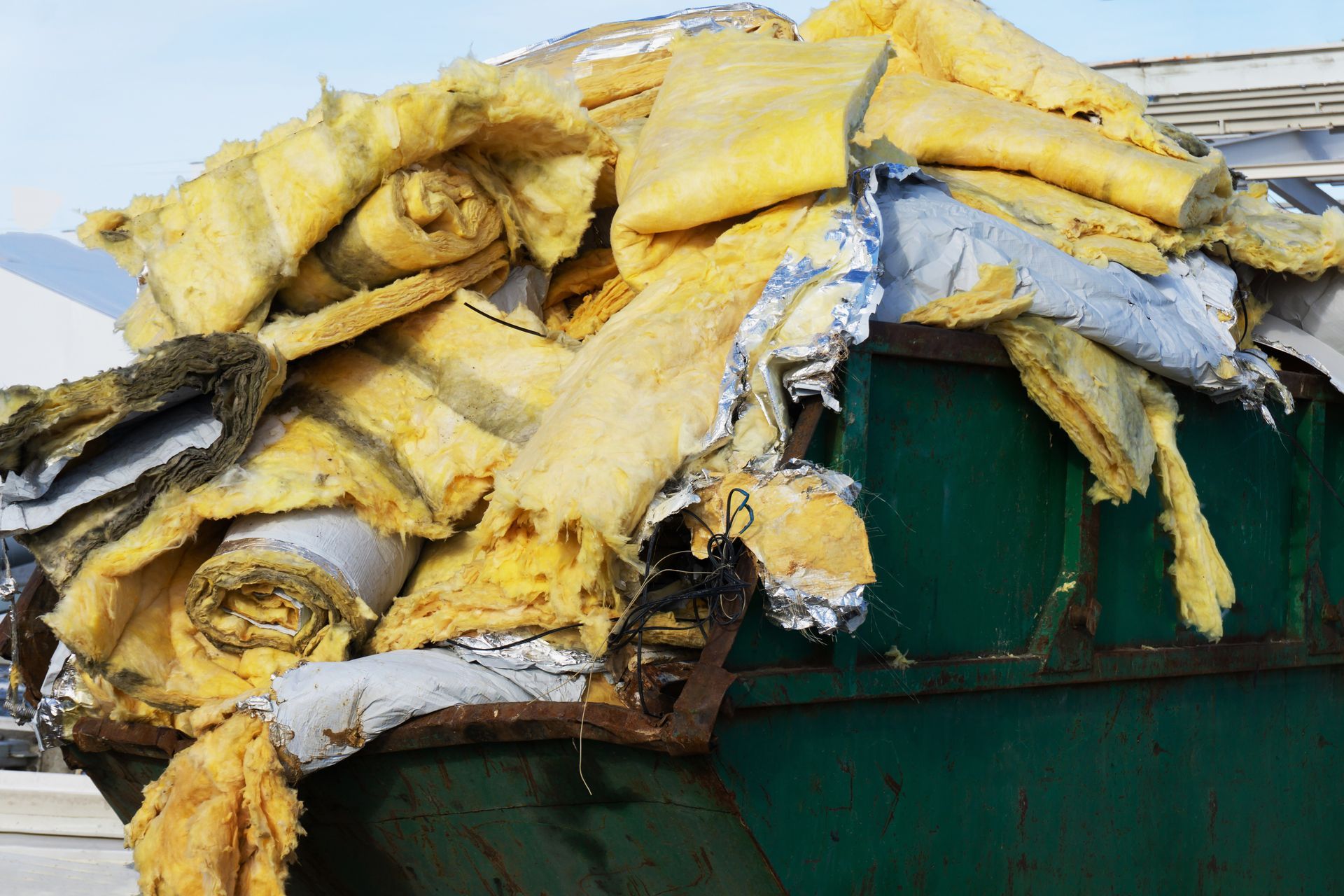 A green dumpster filled with a pile of yellow insulation.
