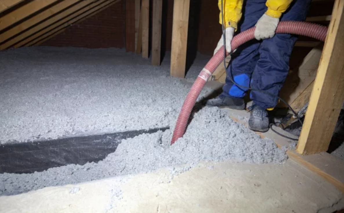 A man is blowing insulation into an attic with a hose.