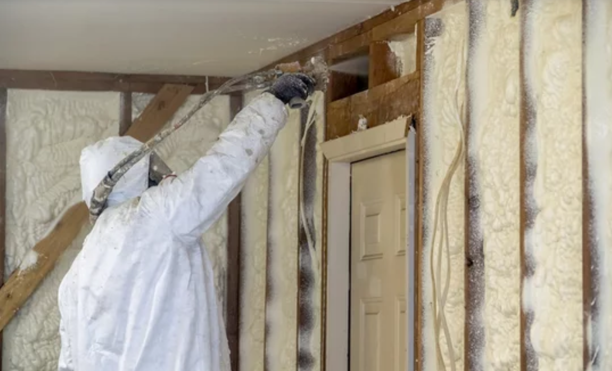 A man is spraying foam insulation on a wall.