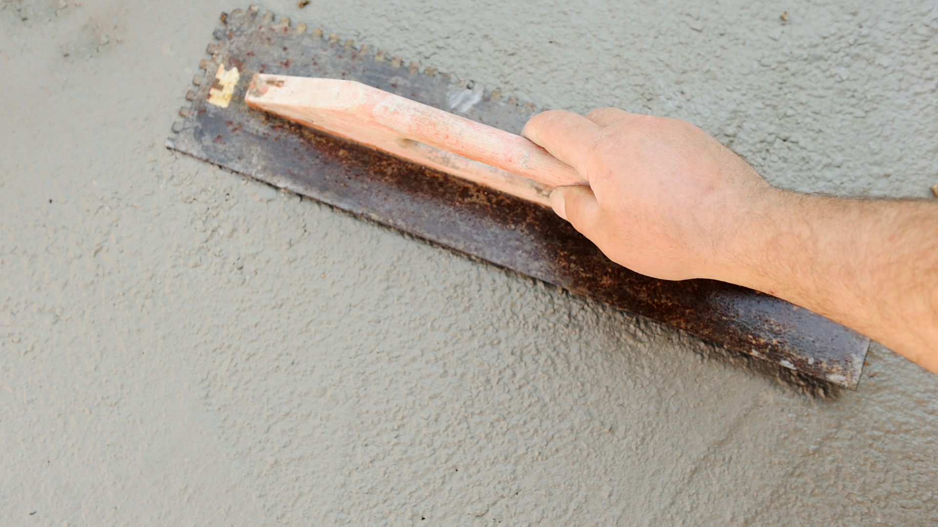 A person is using a trowel to spread concrete on a wall.