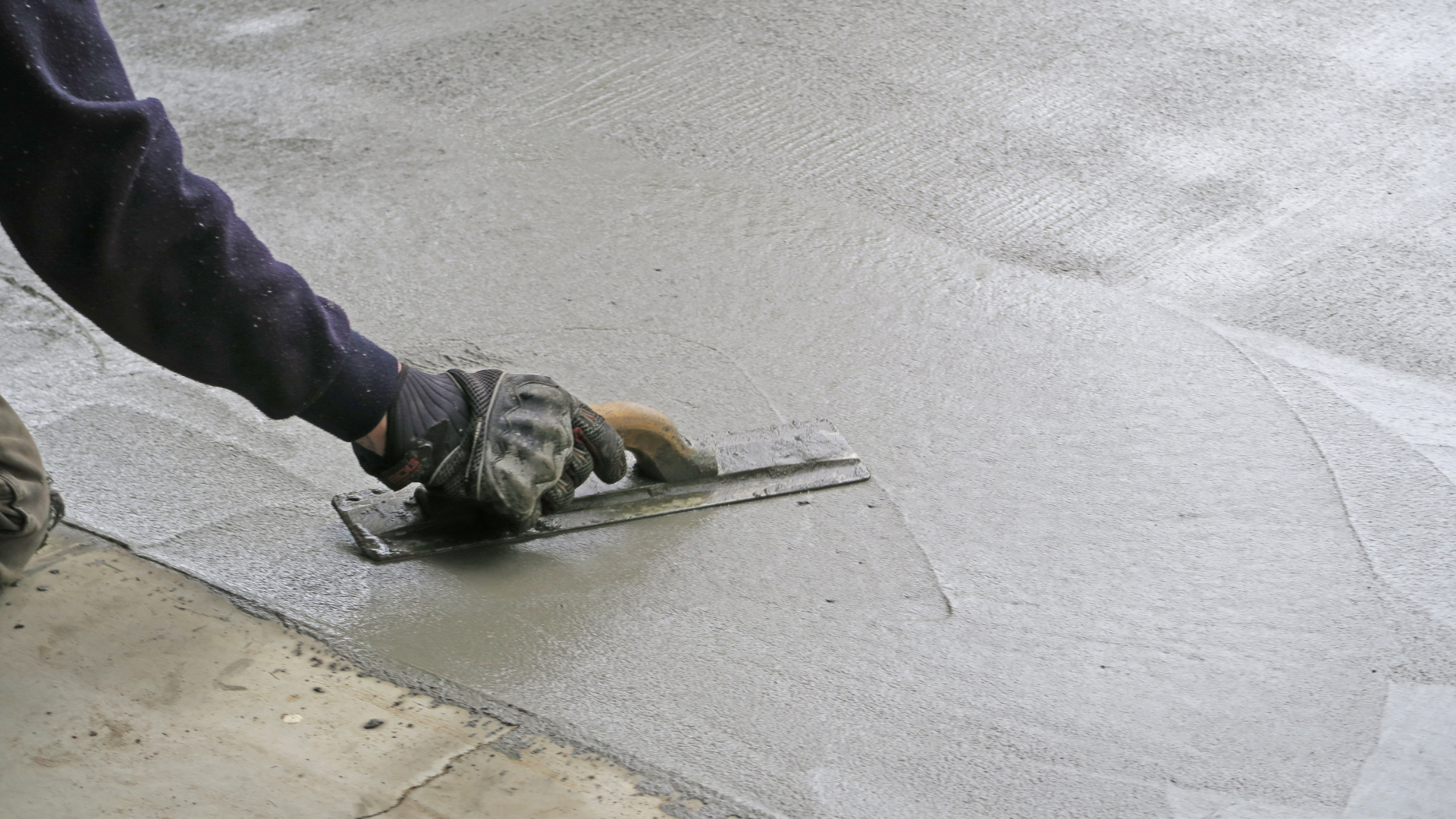 A person is using a trowel to spread concrete on the ground.