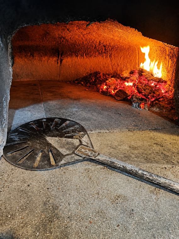 Forno a legna con fiamme ardenti e pala per pizza in metallo sul piano di lavoro.