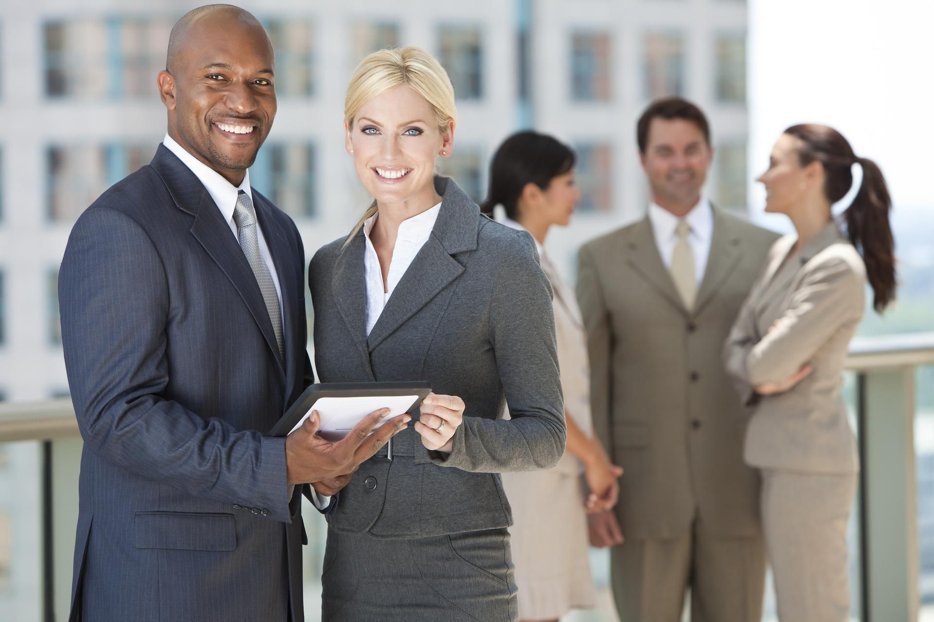 Businesspeople smiling outdoors, man holding tablet, others in background.