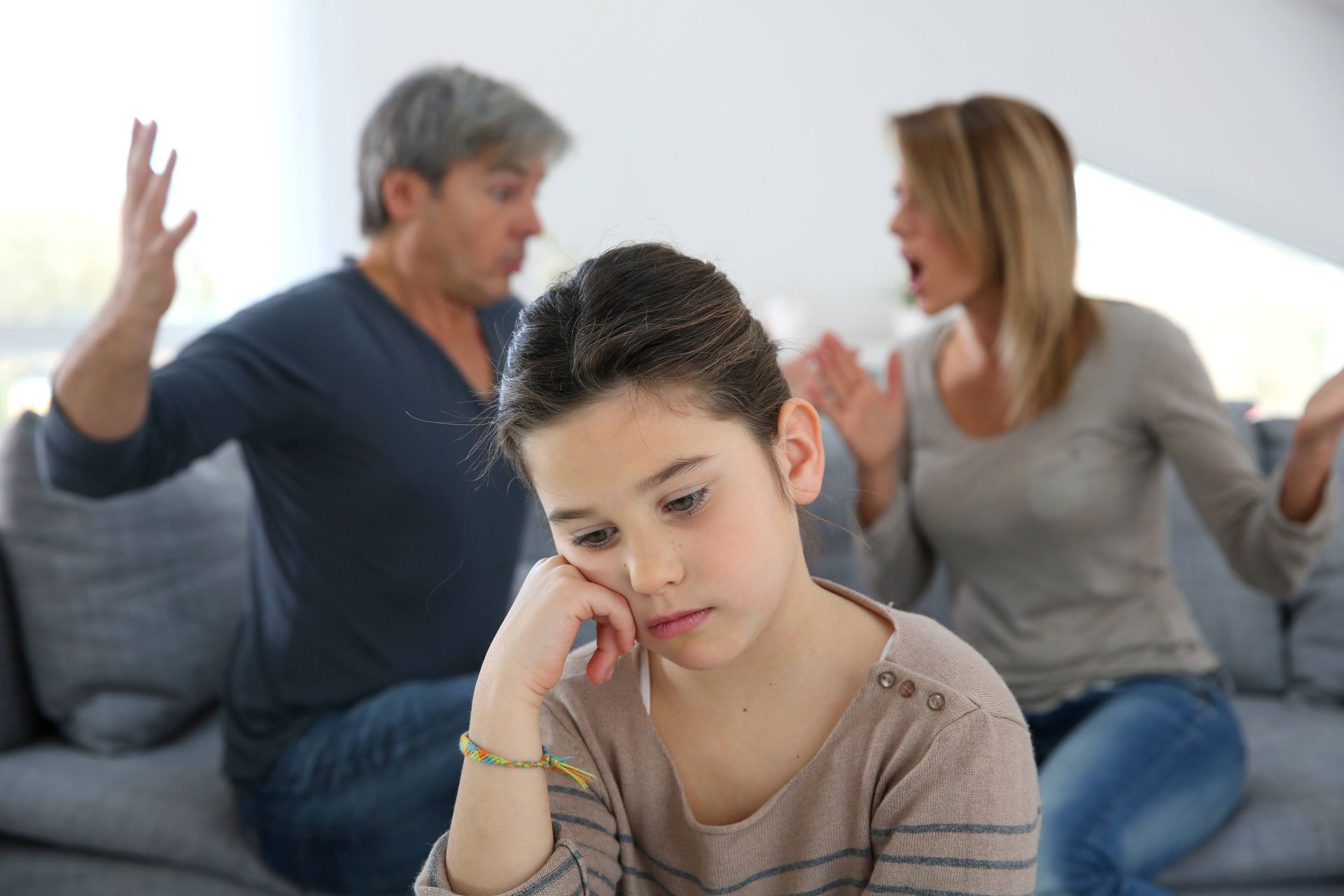 Girl looks sad as parents argue. They are in a living room.