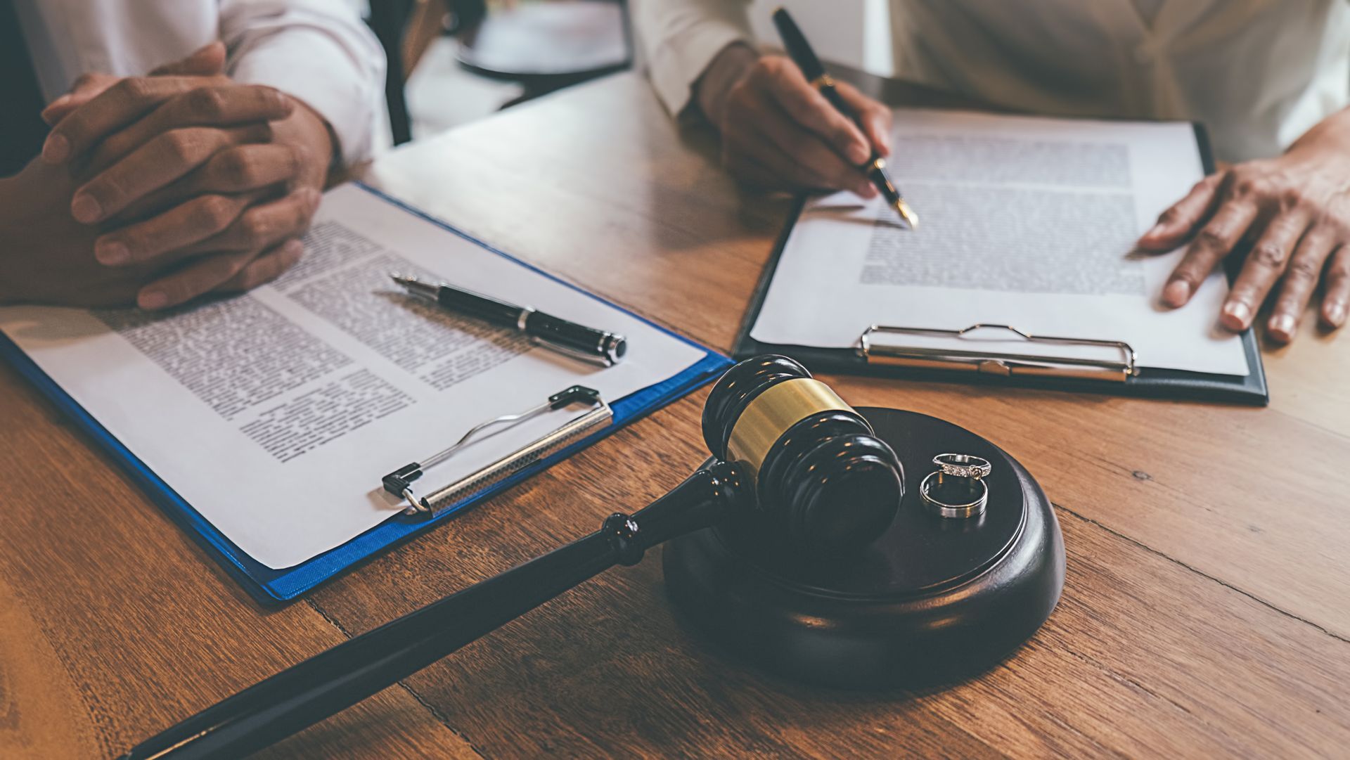 Gavel and signed documents on desk as people review legal paperwork together. Gavel and signed documents on desk as people review legal paperwork together.