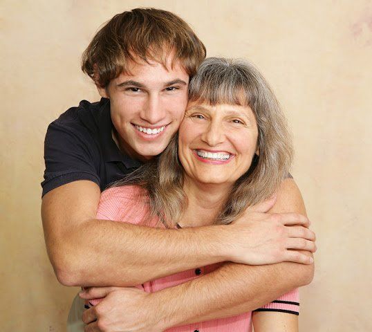 Young man embraces older woman, both smiling widely.