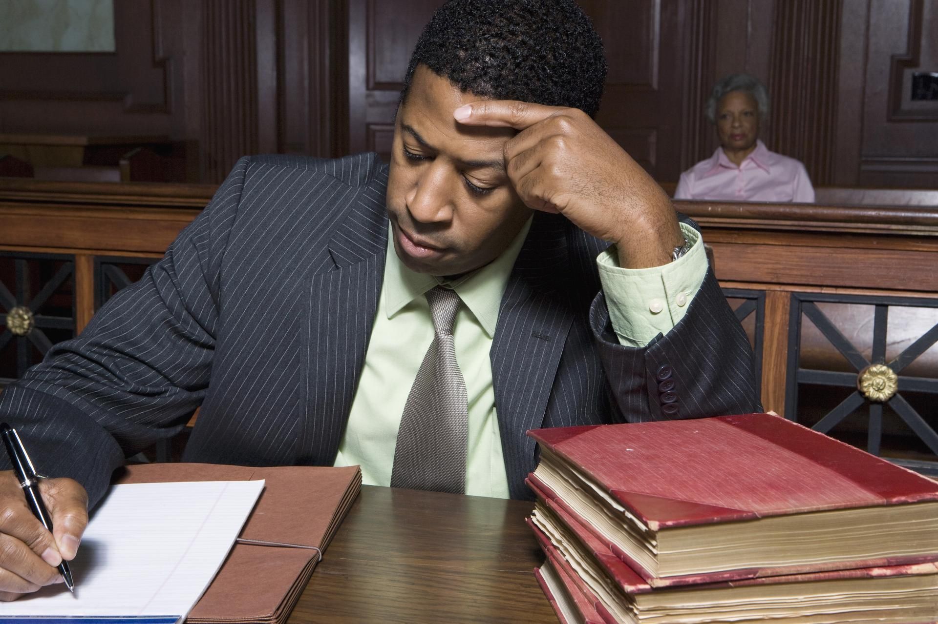 Man in courtroom, writing, appears stressed, with legal books.