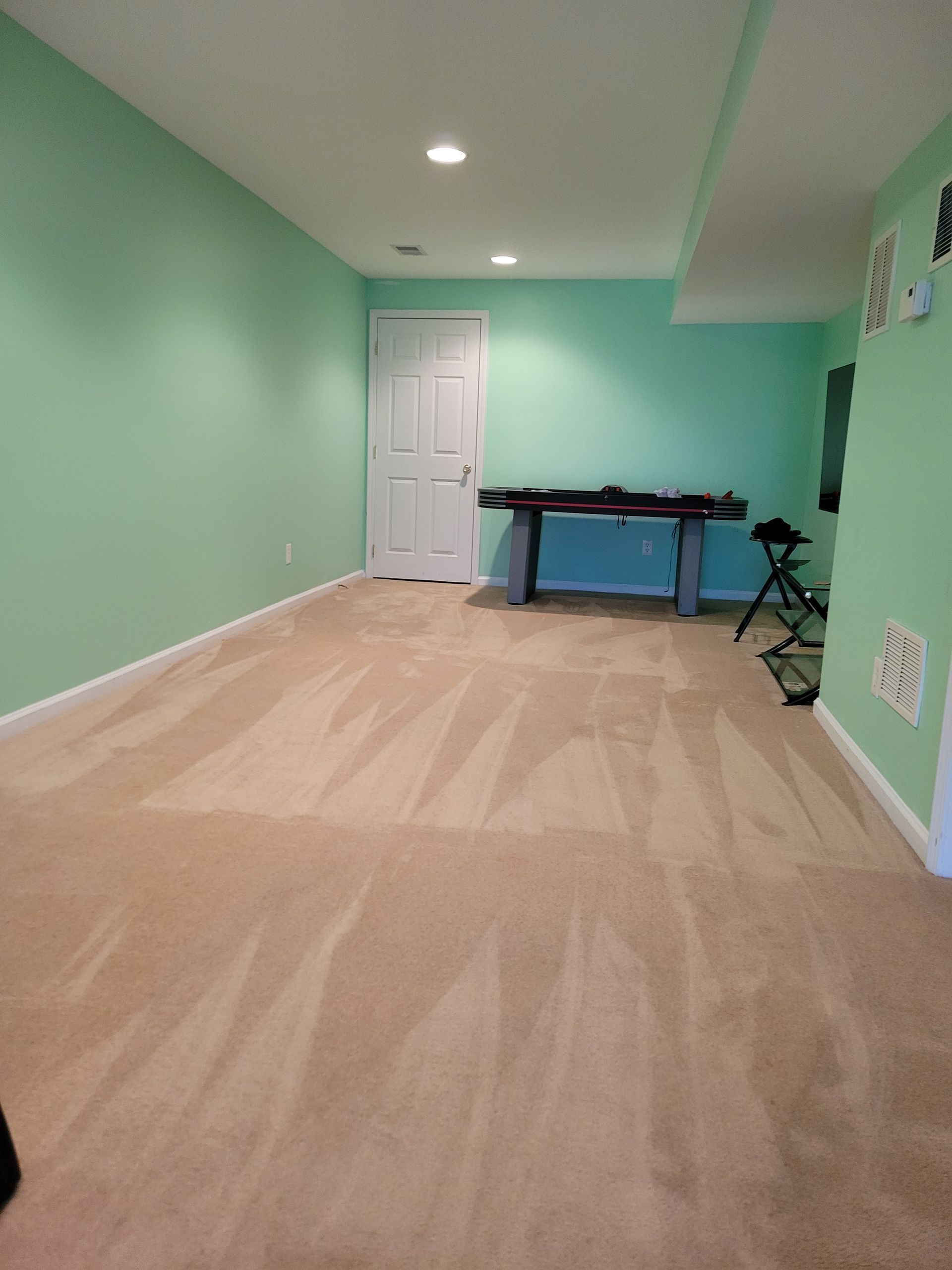 An empty basement with green walls and tan carpet.
