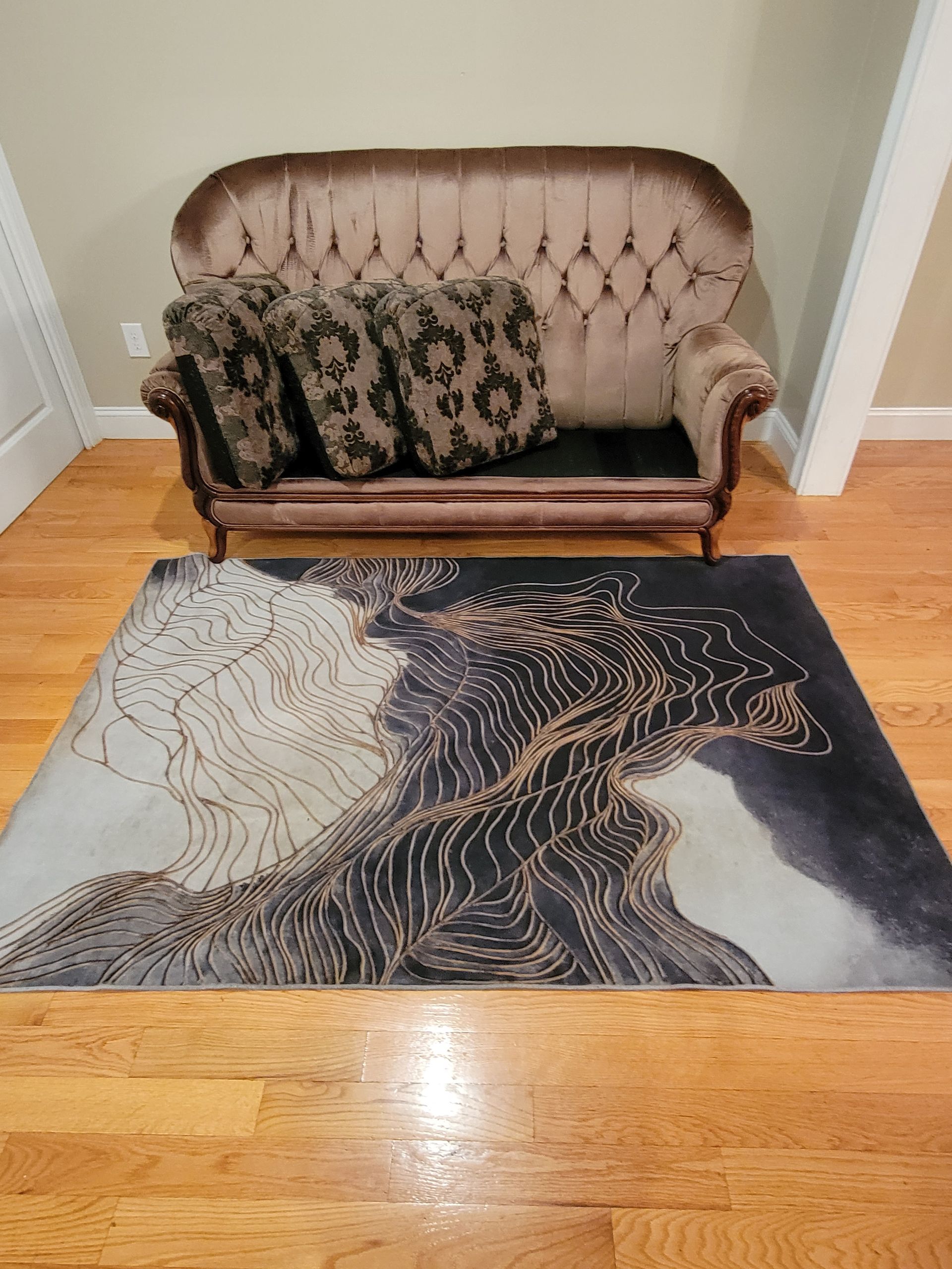 A couch is sitting next to a rug on a wooden floor.