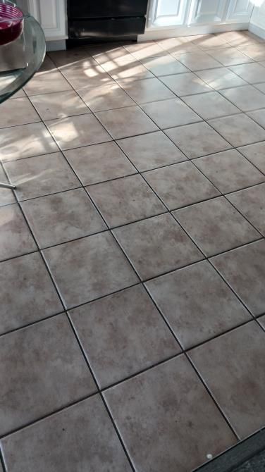 A tiled floor in a kitchen with a glass table in the background