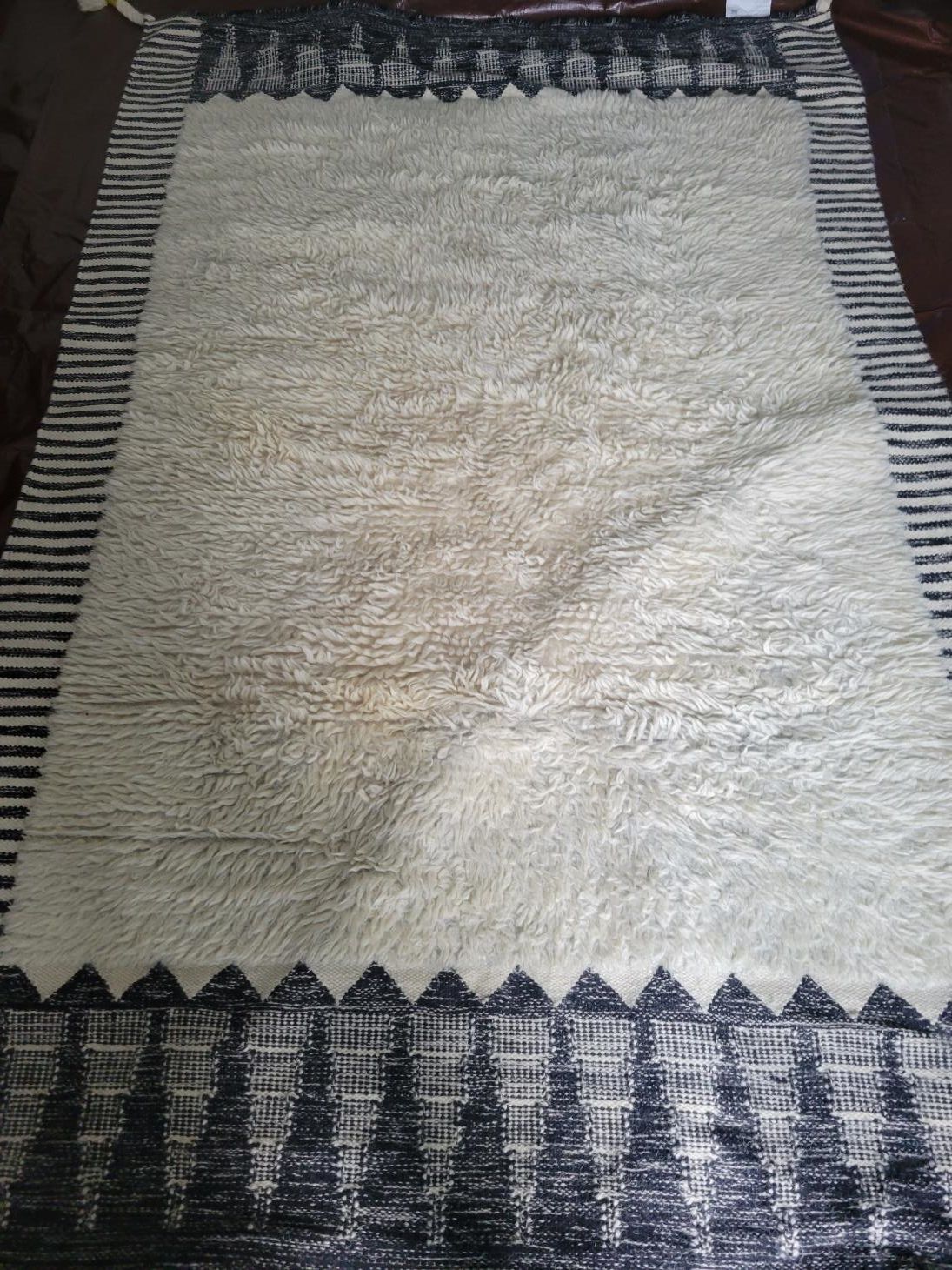 A white rug with a black border is sitting on a wooden floor.