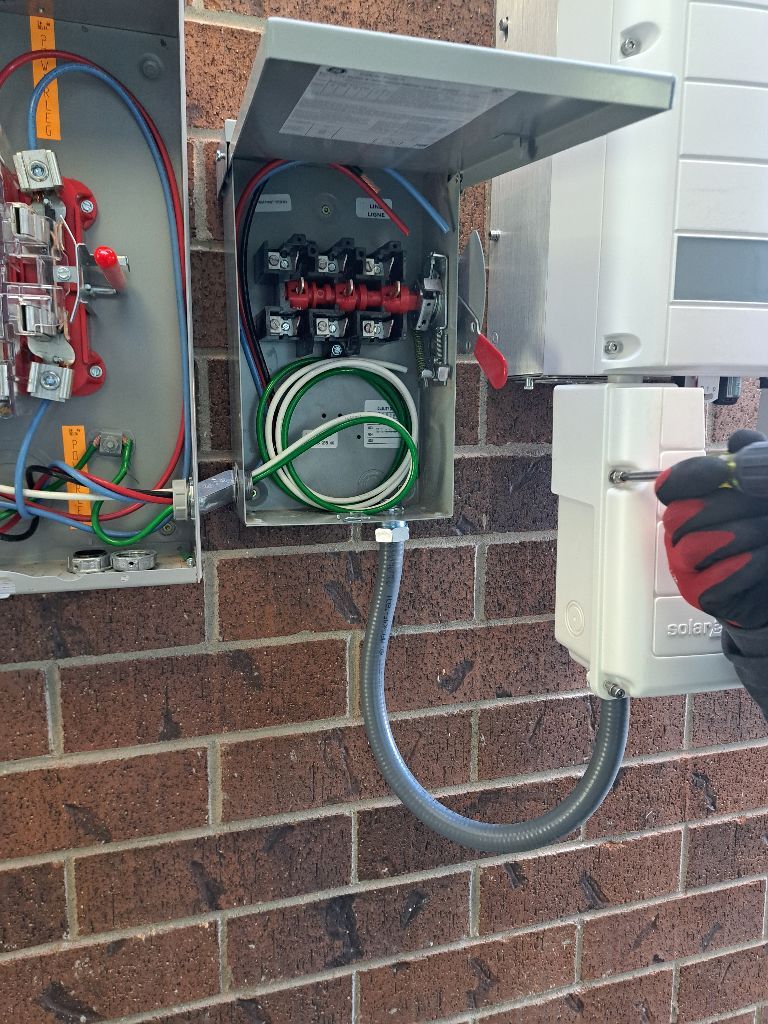 A person is working on a electrical box on a brick wall.