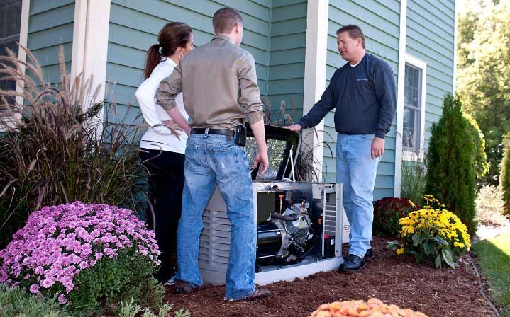 A man and a woman are standing in front of a house looking at a generator.