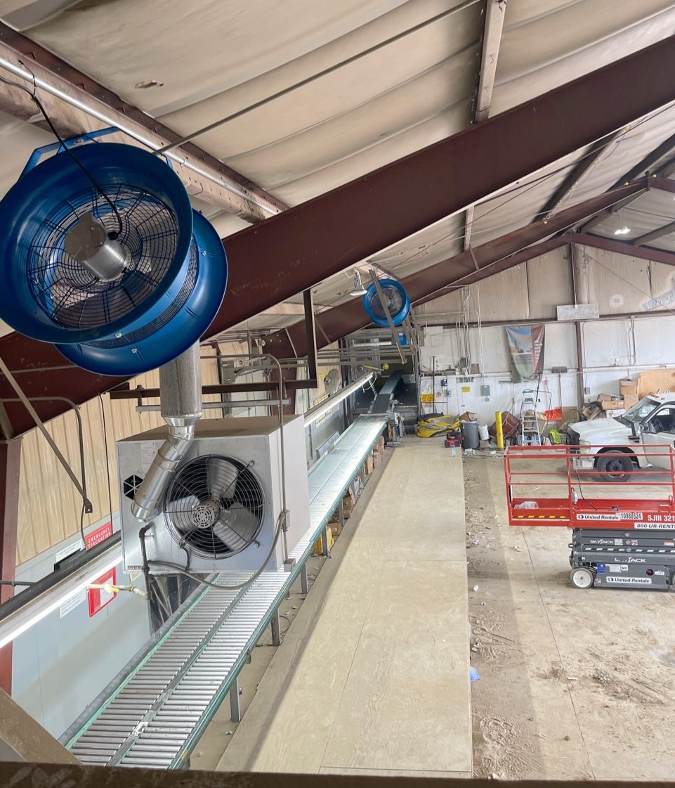 A warehouse with a conveyor belt and fans hanging from the ceiling.