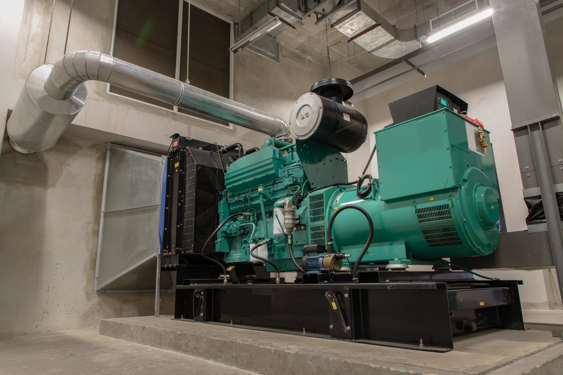 A large, green industrial generator in a concrete room with a metal exhaust pipe.