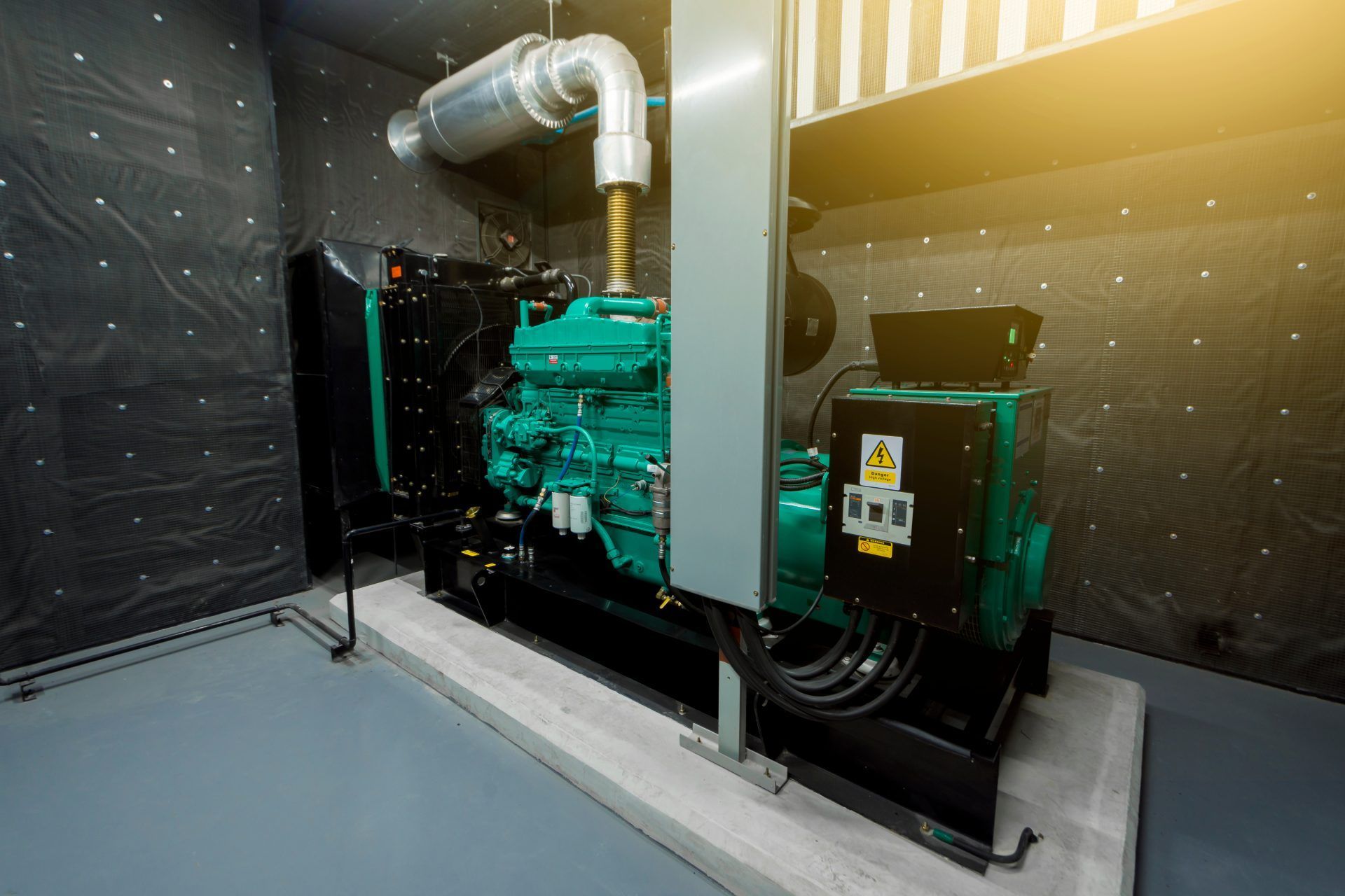 Green and black generator in an enclosed room, gray floor, textured wall, silver exhaust pipe.