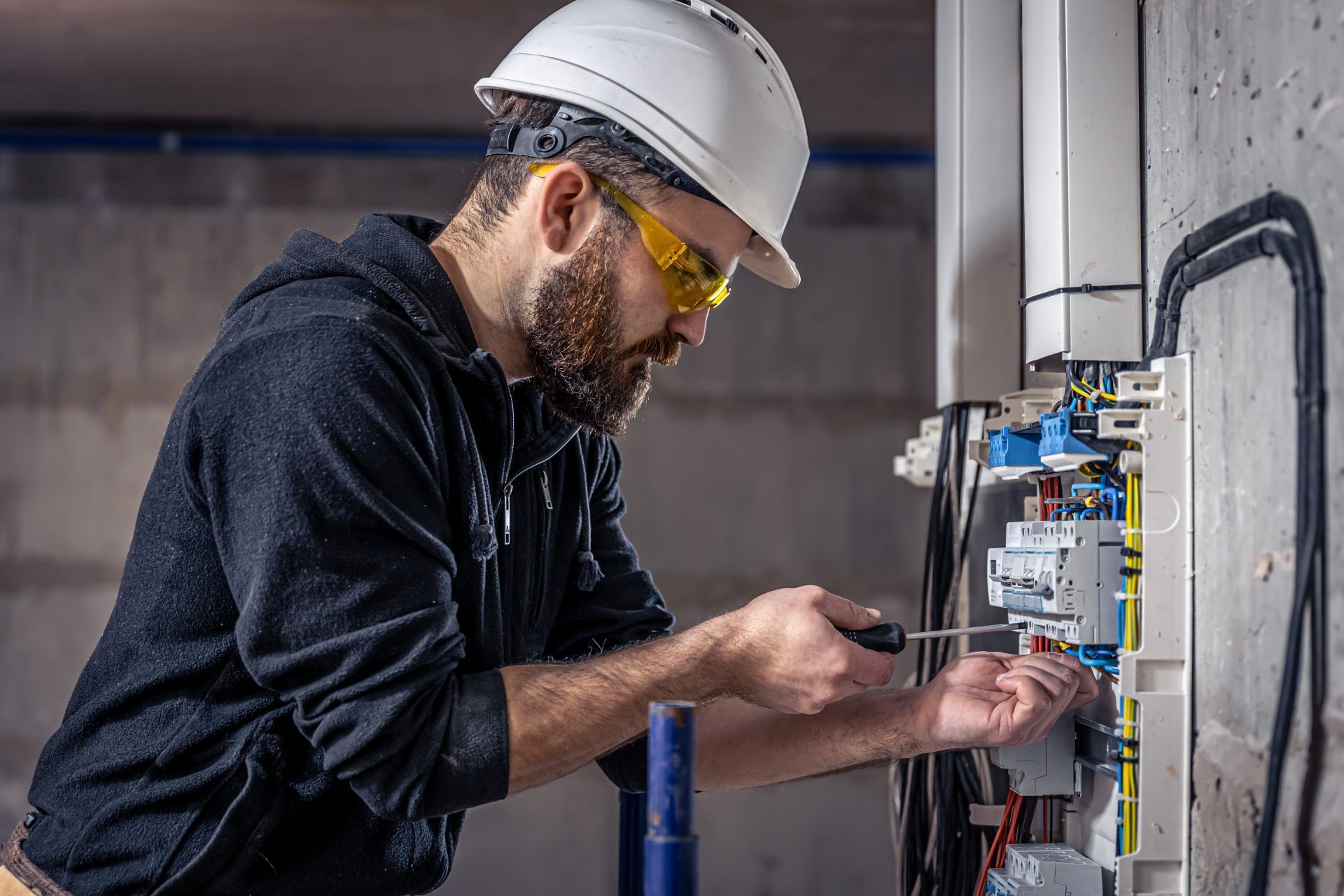 Electrician working on electrical panel, wearing safety glasses and hard hat.