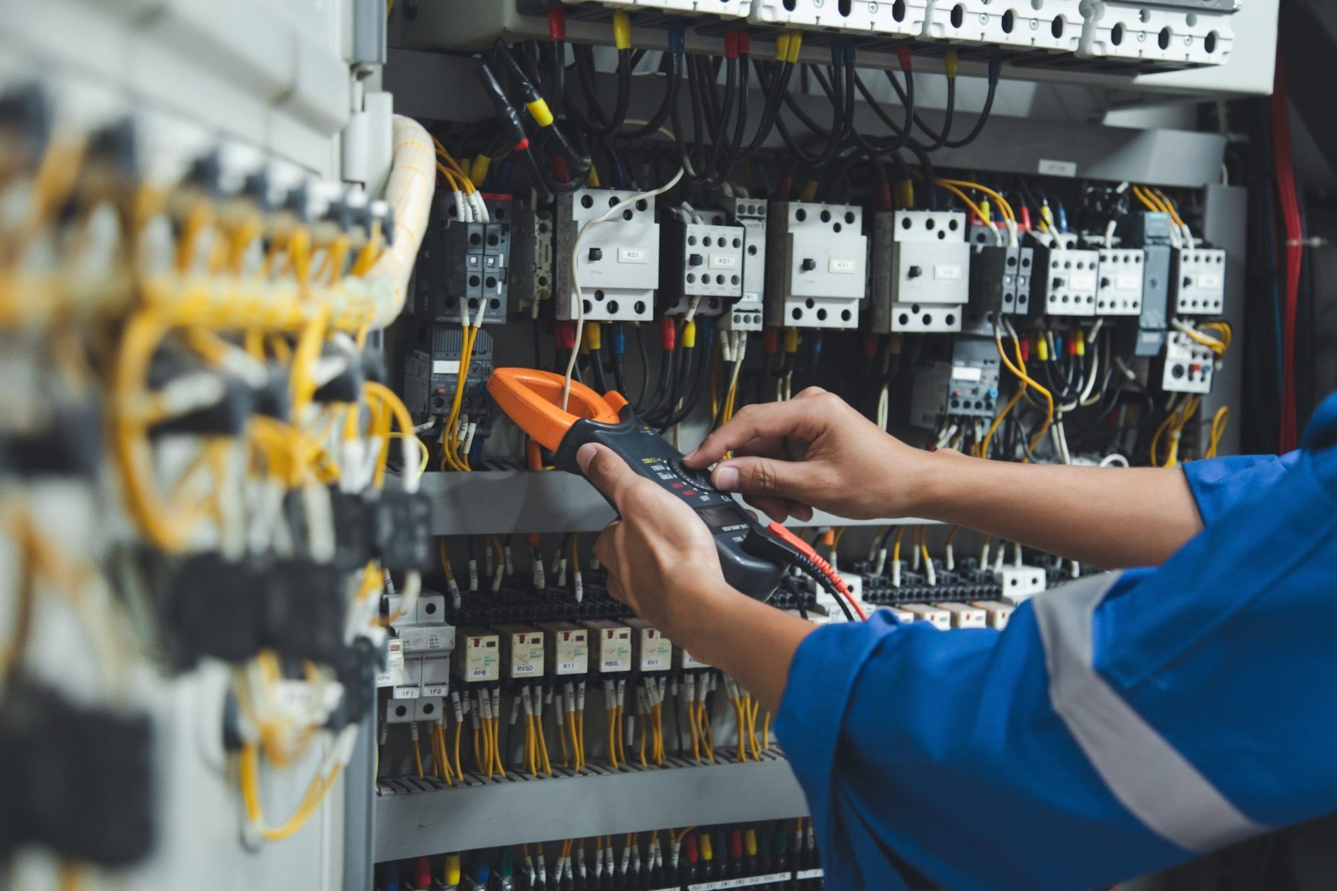 Electrician in blue uniform using a multimeter on electrical panel.