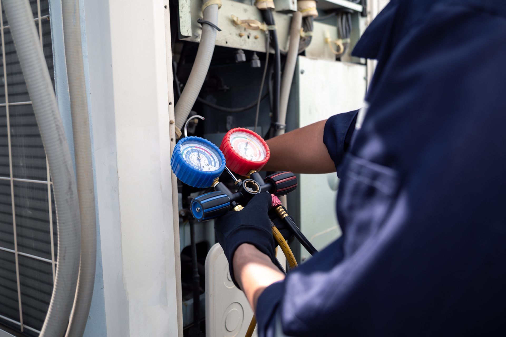 HVAC technician connecting gauges to an air conditioning unit. Hands in black gloves.