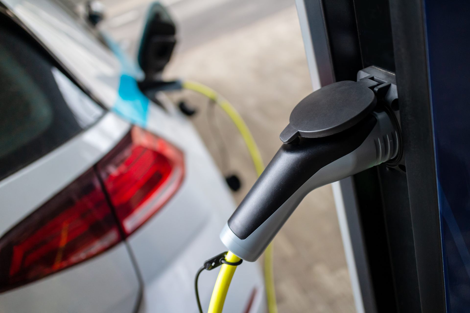 Electric car charging with a cable plugged into the vehicle, a yellow cord, and black and grey charging station.