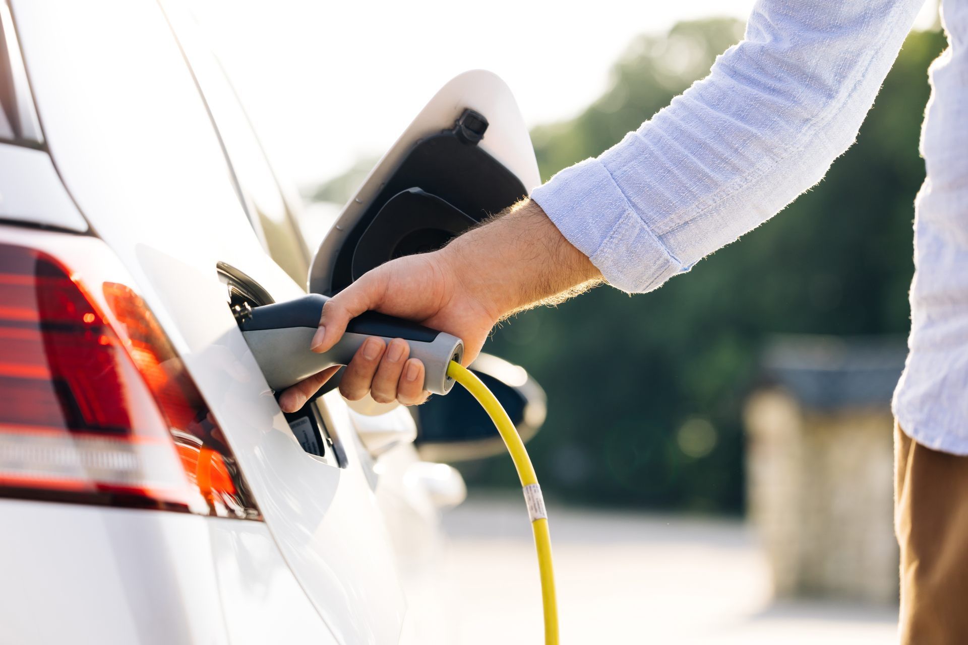 Person plugging in electric car with a yellow charging cable.