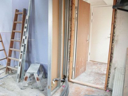 Interior renovation in progress, doorway with a wooden door, ladder, and tools.
