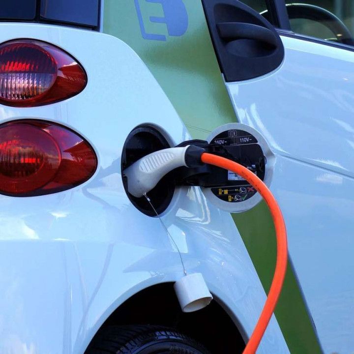 White electric car charging, with orange cable plugged into the charging port.