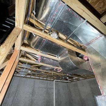 HVAC ductwork in attic, with wooden beams and concrete walls.