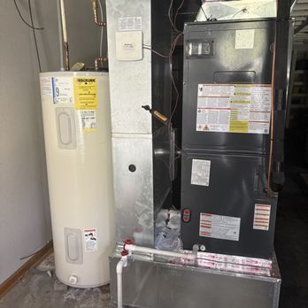 A water heater and furnace stand side-by-side against a wall in a basement.