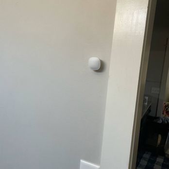 White smart home device mounted on a light-colored wall next to a doorway.